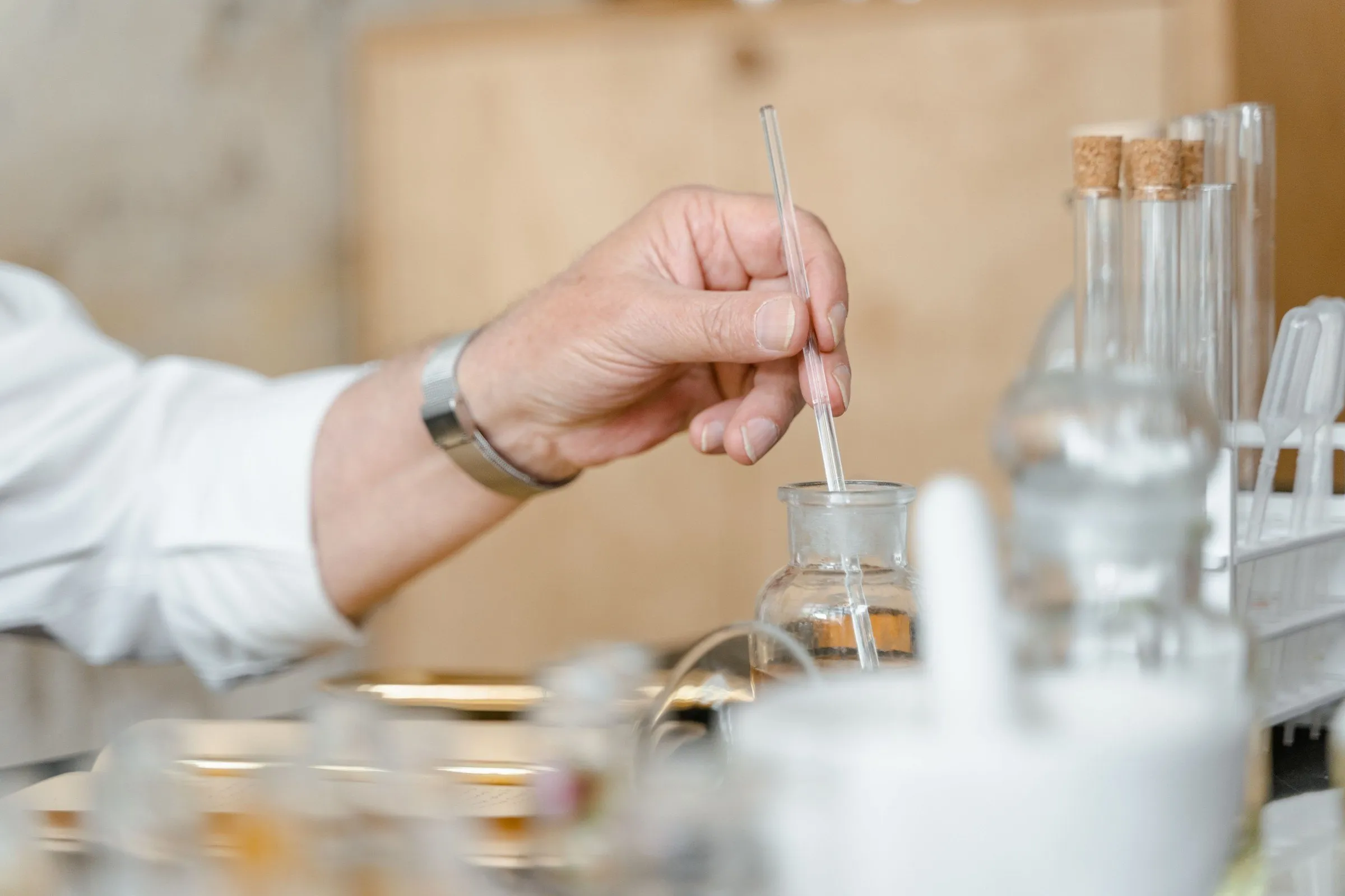 The perfumer's hand holding a glass pipette over a small bottle on the bench