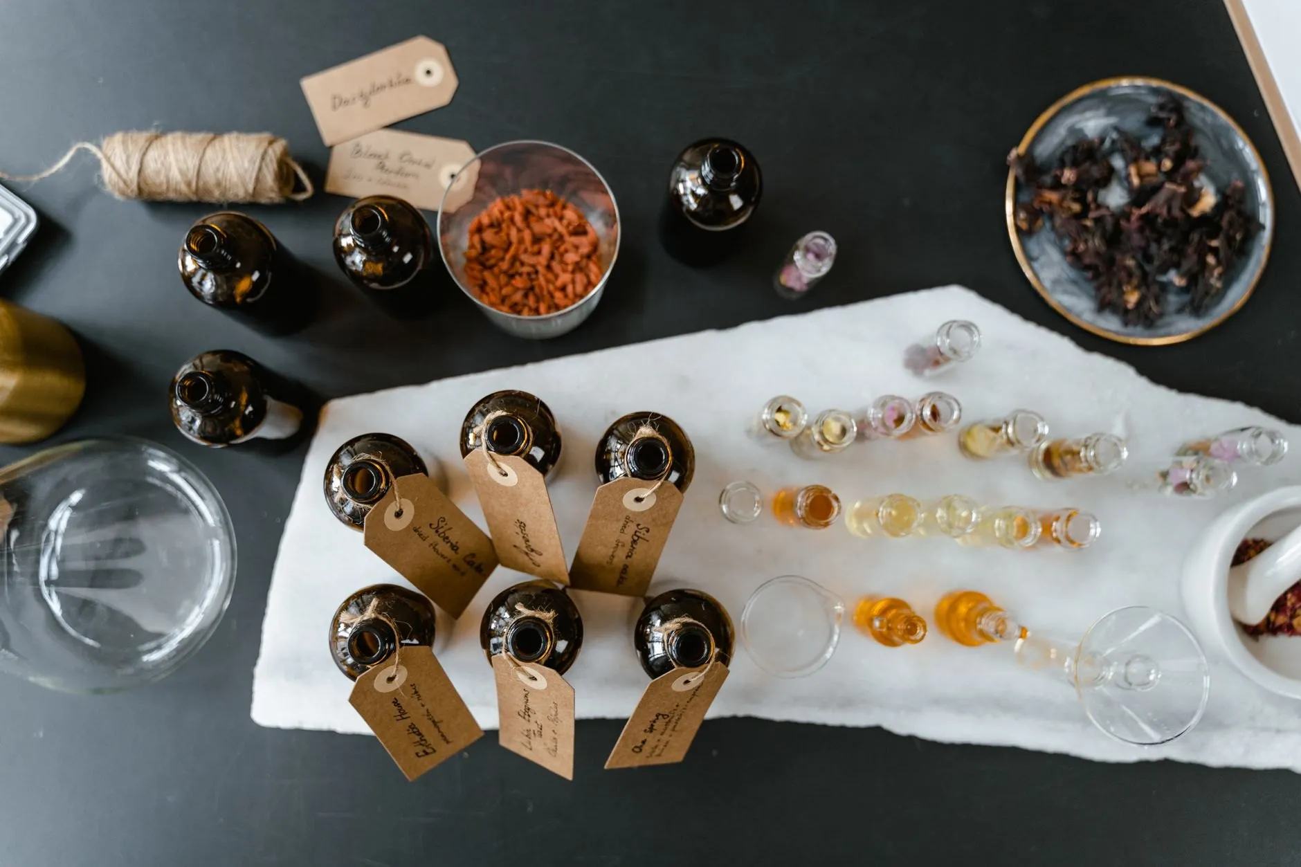 Amber bottles with handwritten tags laid out on a marble slab, seen from above