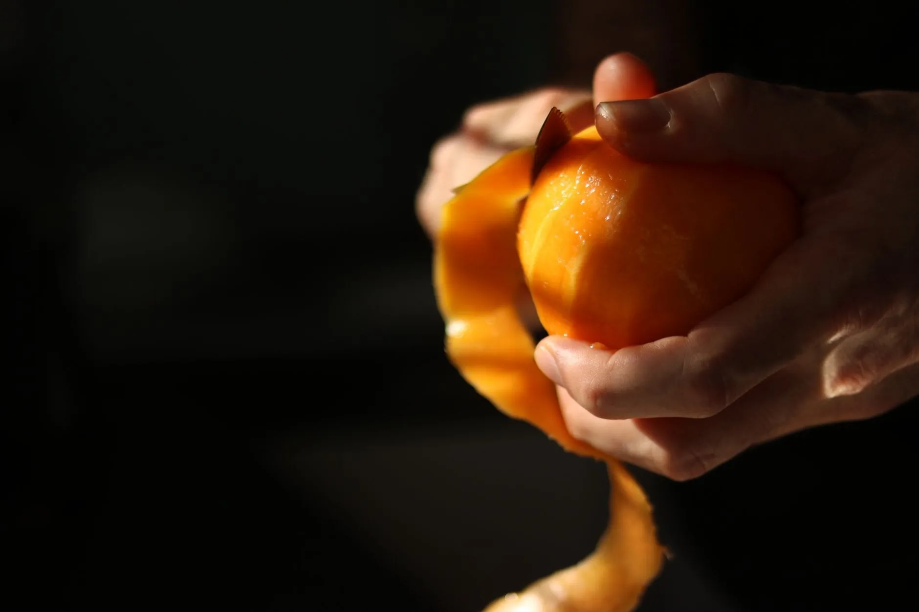 Hands peeling a citrus fruit in one long spiral