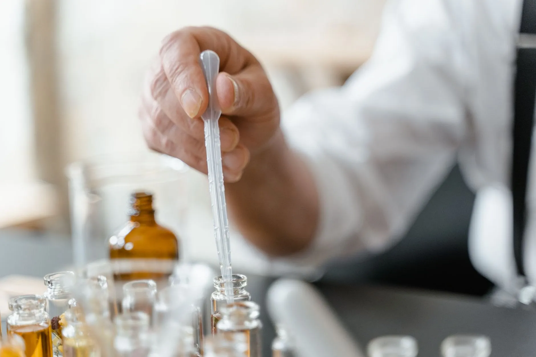A glass pipette held above rows of small fragrance vials